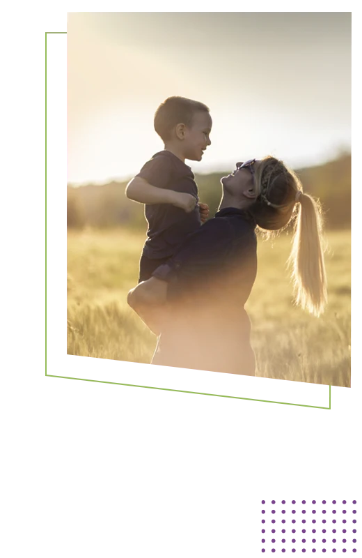 Adult lifting a child in an open field with warm sunlight, creating a relaxed outdoor family moment.