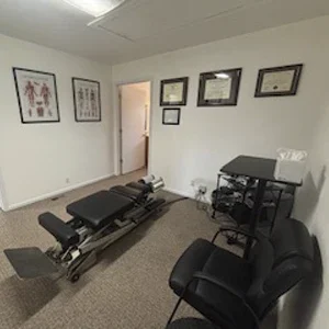 Chiropractic treatment room featuring an adjustment table, anatomical charts, and framed certificates.