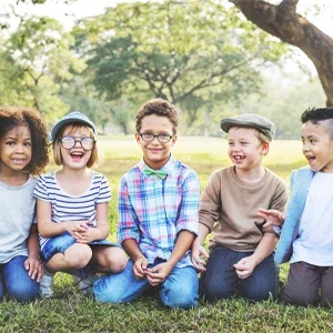 Group of children sitting together outdoors on the grass, enjoying a bright and open natural setting.