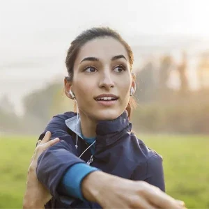 Person stretching an arm outdoors in a grassy field, preparing for physical activity or exercise.